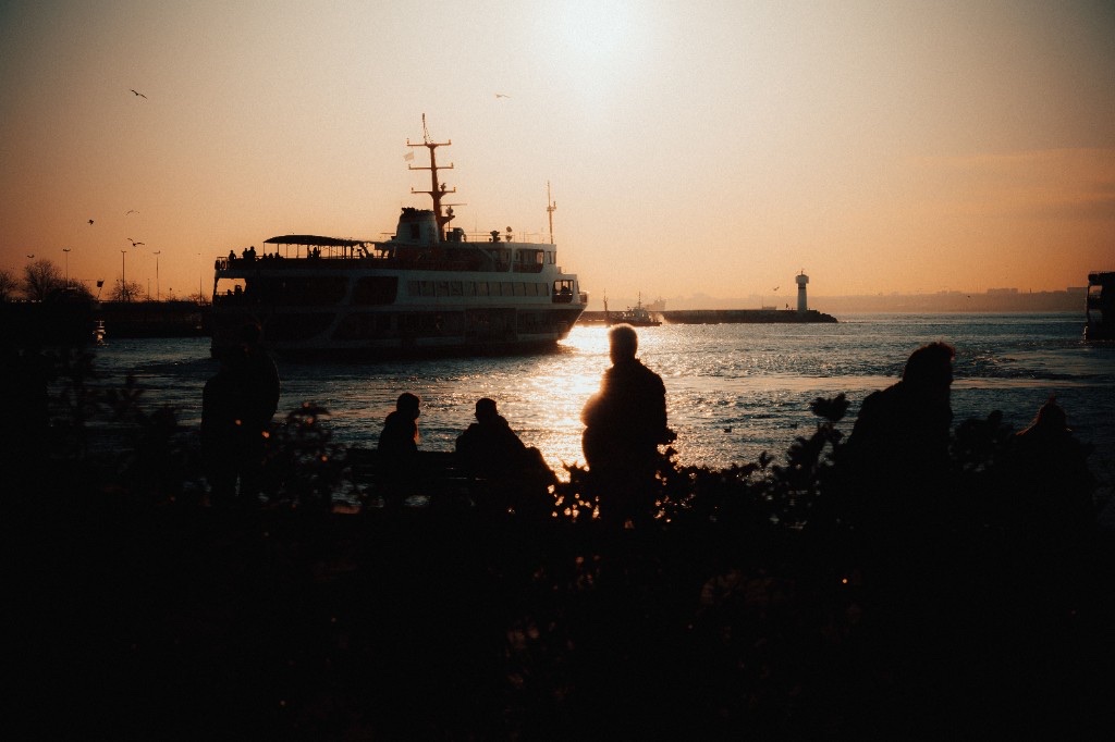 Passenger ferry crossing a harbour at sunset, watched from the shore